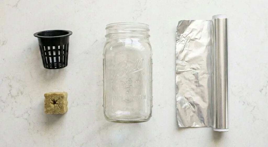 Flat lay of Kratky hydroponic supplies including a 32-ounce Mason jar, net cup, rockwool cube, nutrients, and pH kit on a kitchen counter